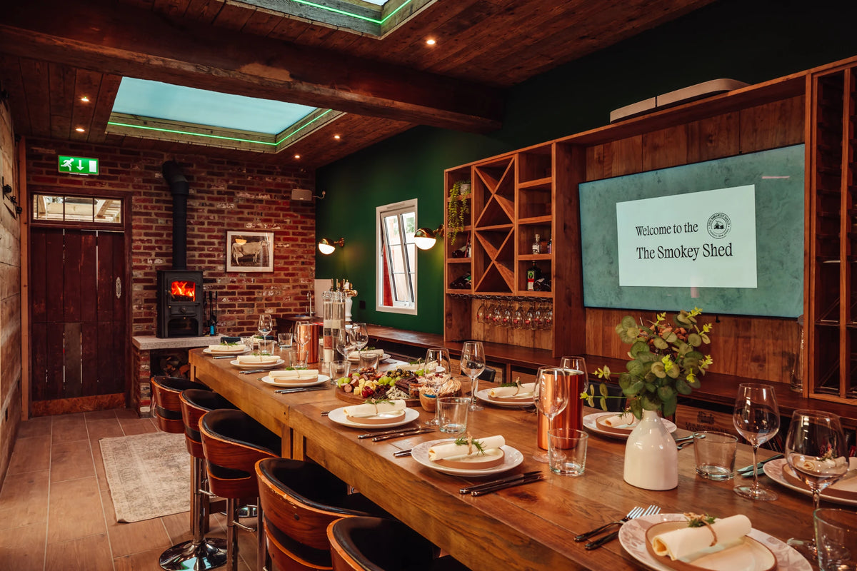 The Smokey Shed dining room, with the long oak table laid for dinner and the wood burner lit